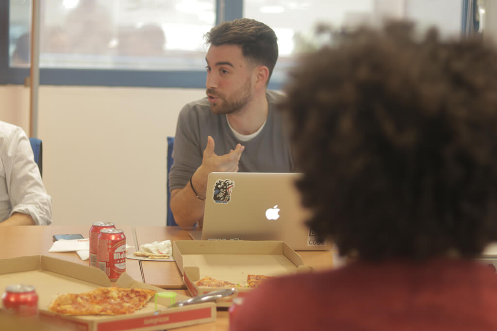 Compañero de BABEL con portátil hablando en un afterwork con pizzas en la mesa