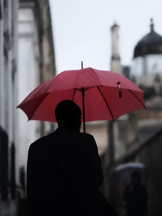 Hombre con paraguas rojo paseando por la calle