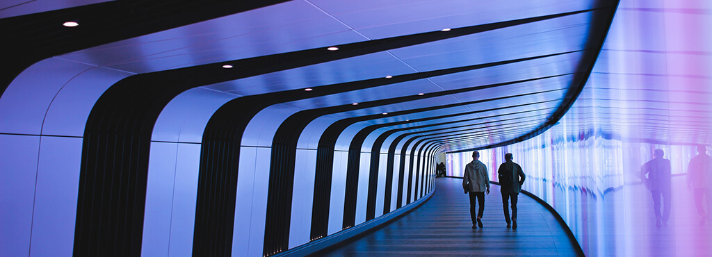 dos personas caminan en un túnel con aspecto futurista y luces azules