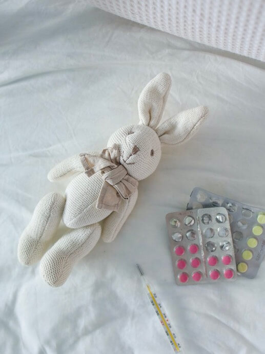 Babel Salud DKV.  Un conejo de peluche encima de una cama rodeado con un termómetro y pastillas