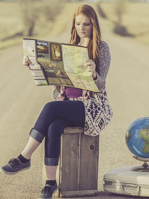 Babel Transportes Alsa. Mujer sentada encima de una maleta mirando un mapa