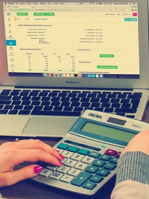 Administración Tributaria. Mujer utilizando una calculadora con un portátil de fondo